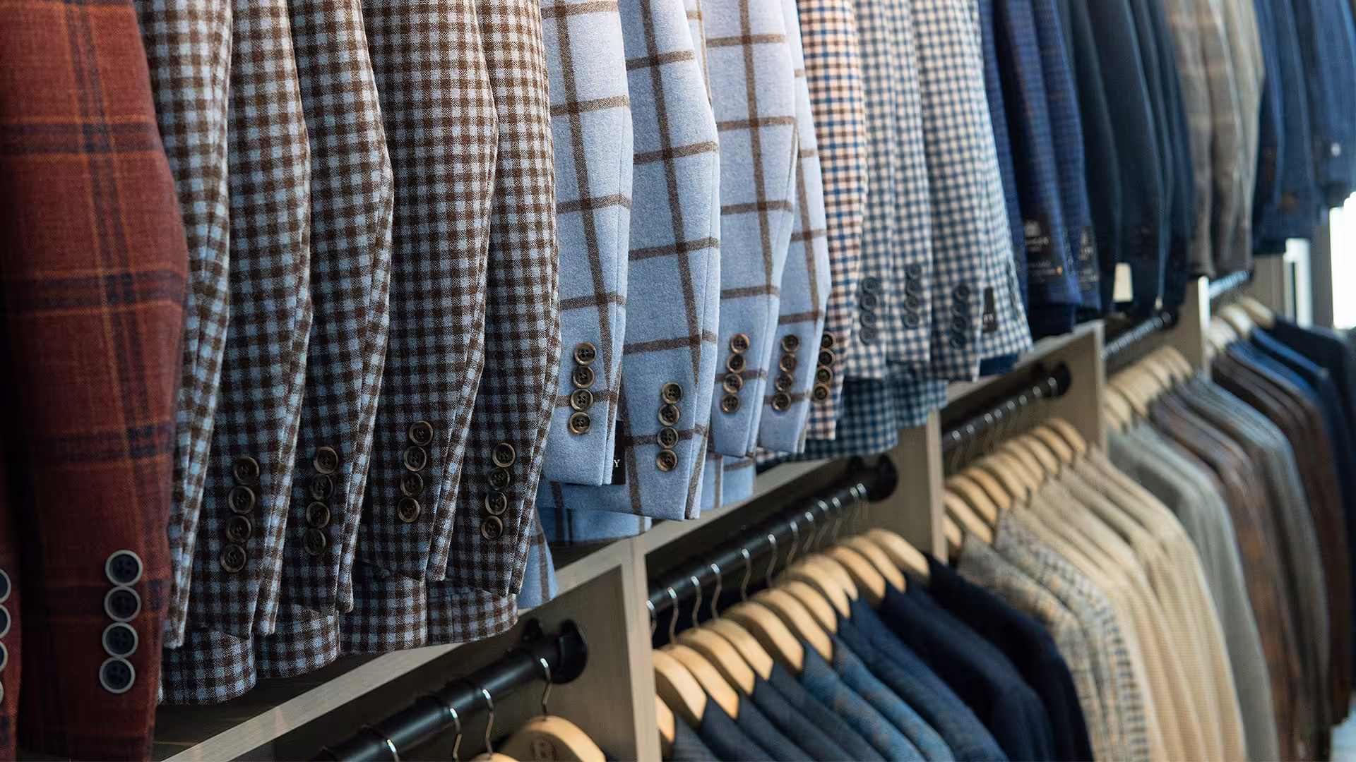 Rows of patterned men’s blazers and jackets hanging on wooden hangers in a retail store.