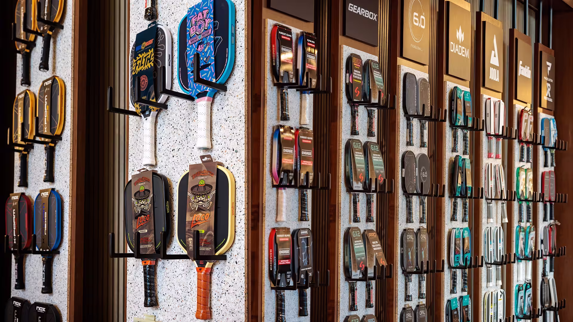 Wall display of various colorful pickleball paddles hanging in rows in a store.