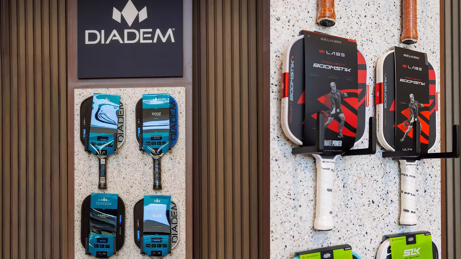 Display with four blue Diadem pickleball paddles on wood and four Selkirk Project Boomstik paddles on white wall.