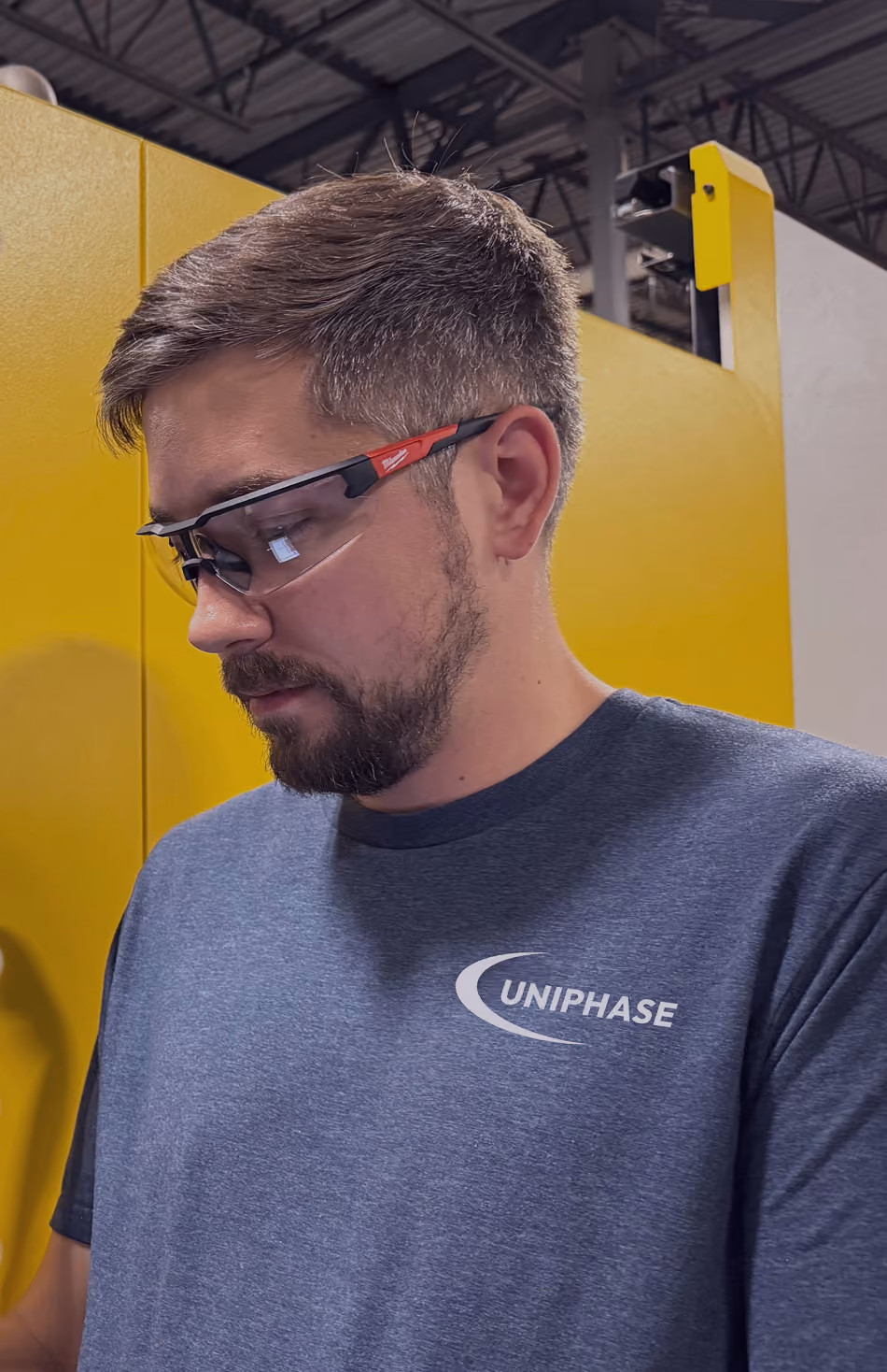 Uniphase employee wearing safety glasses and a Uniphase branded shirt on the factory floor
