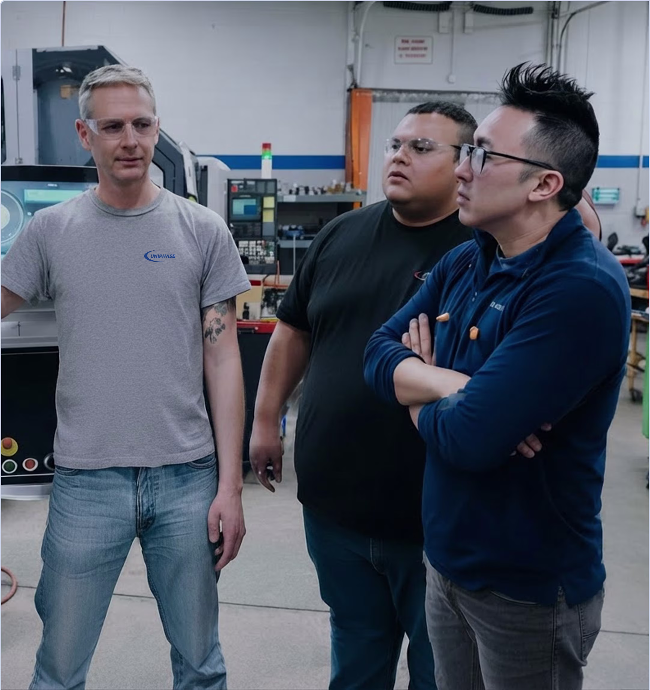 Employee demonstrating a CNC machine control panel to three coworkers on the shop floor