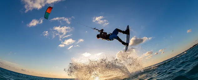 Kitesurfer catching air above ocean waves at sunset