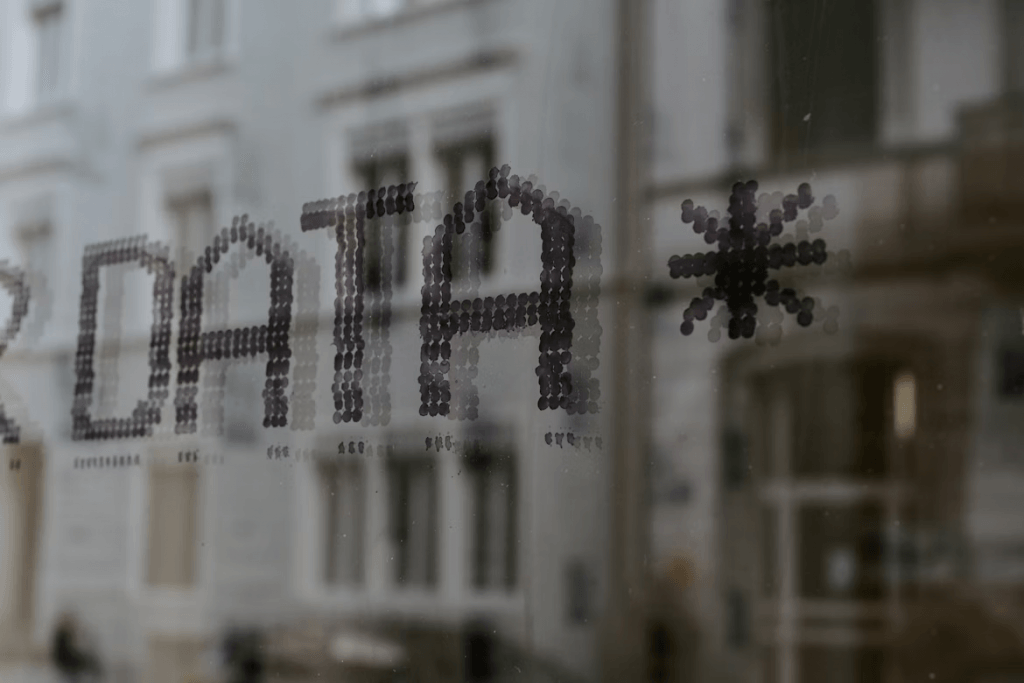 Decorative photograph of the word DATA spelled out in small dots on a window, with a blurred building behind it.