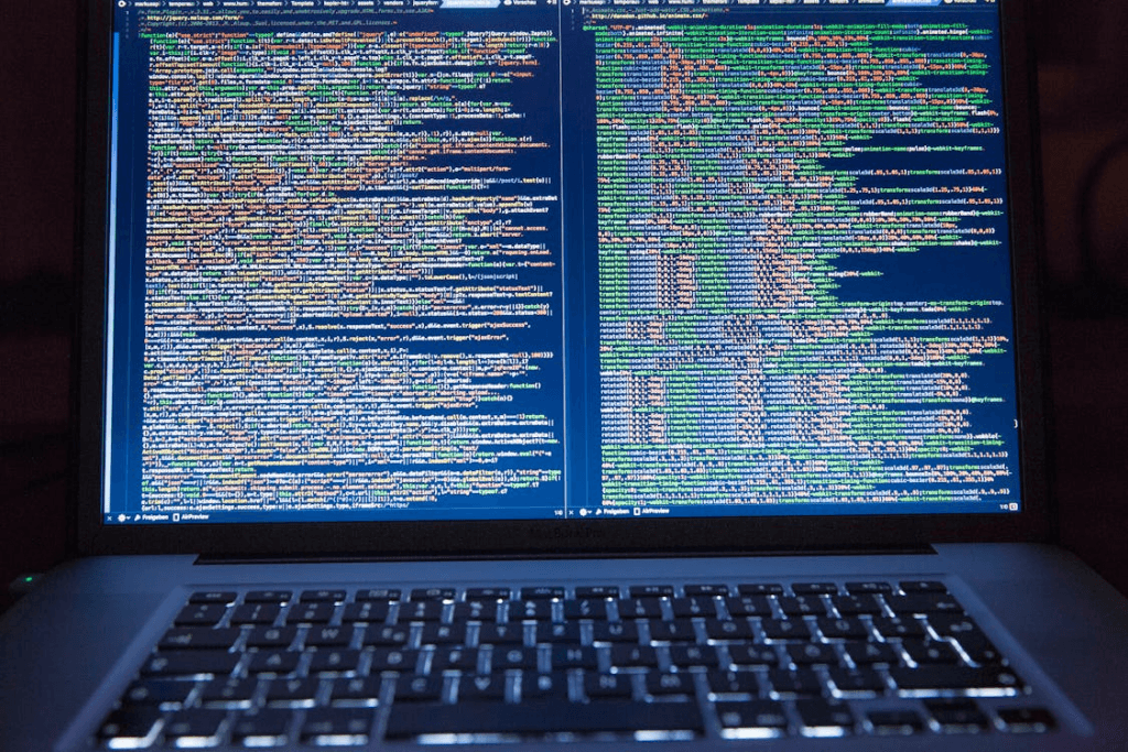 Decorative photograph of an open laptop displaying two columns of dense, colour-highlighted code.