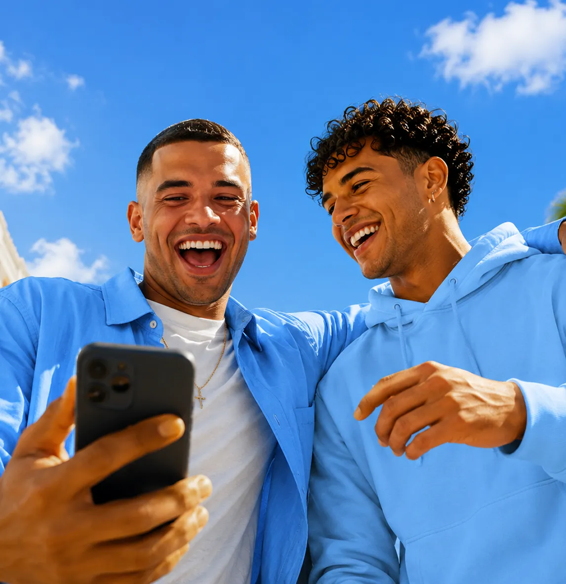 Two smiling young men looking at a mobile phone together under a clear blue sky.