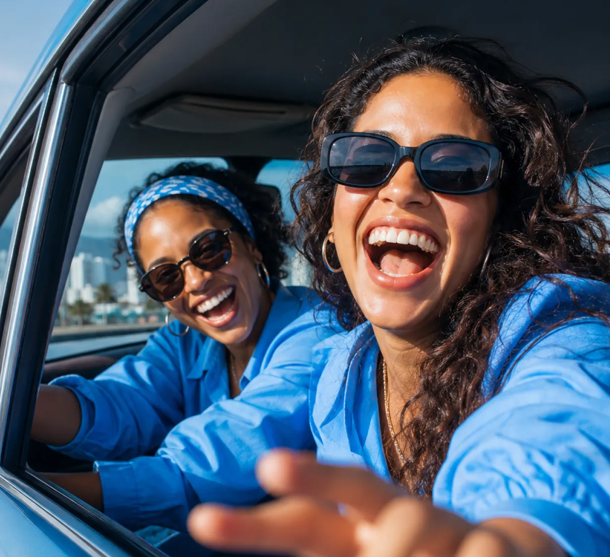 Two smiling women wearing sunglasses are in a car, showing joy and fun.