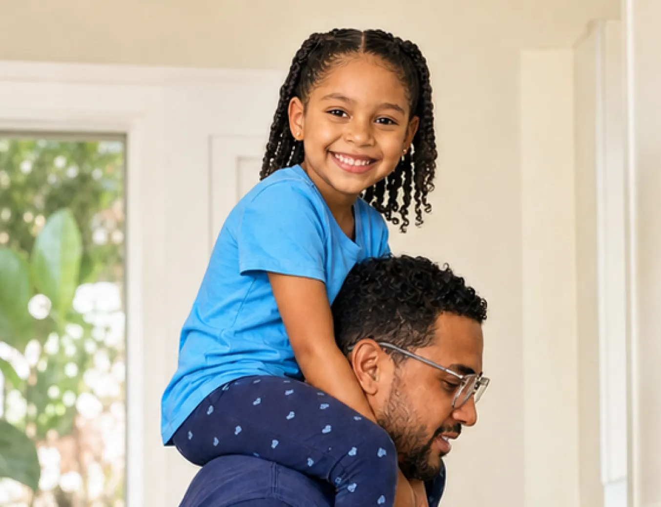 Smiling girl in a blue t-shirt sitting on the shoulders of a man wearing glasses.