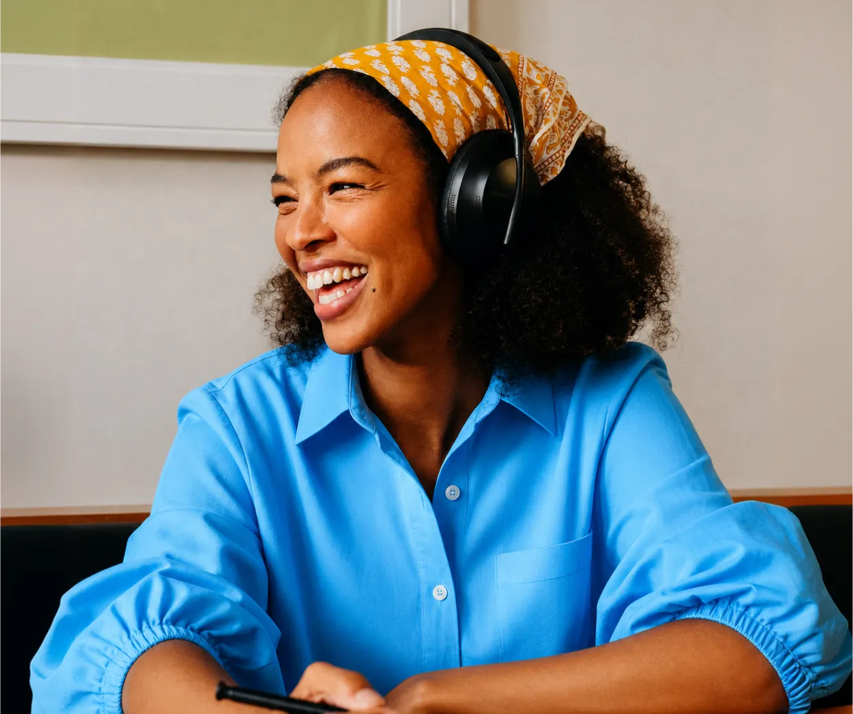 Smiling woman wearing black headphones and a yellow headscarf, wearing a blue shirt.