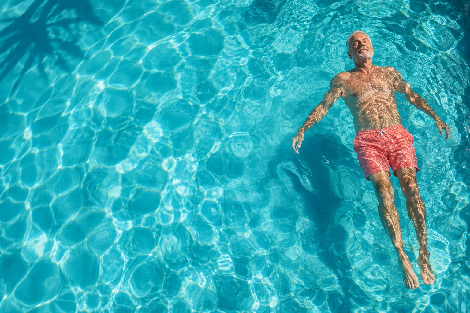 Older man floating in turquoise pool water