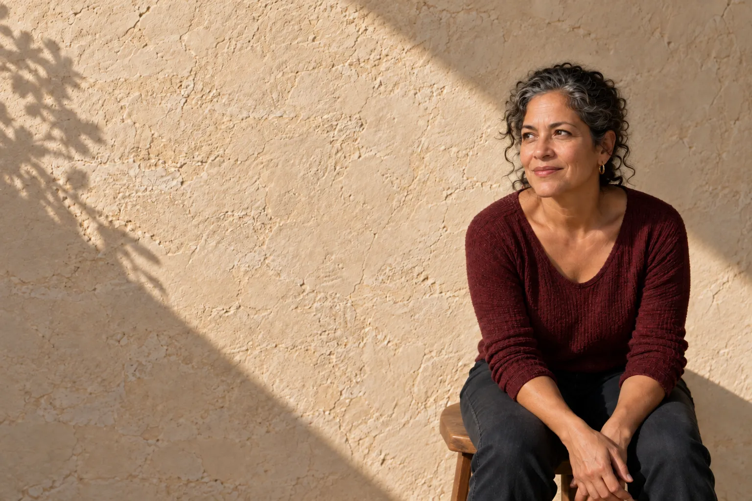 Woman in a burgundy sweater seated against limestone, looking naturally off-camera