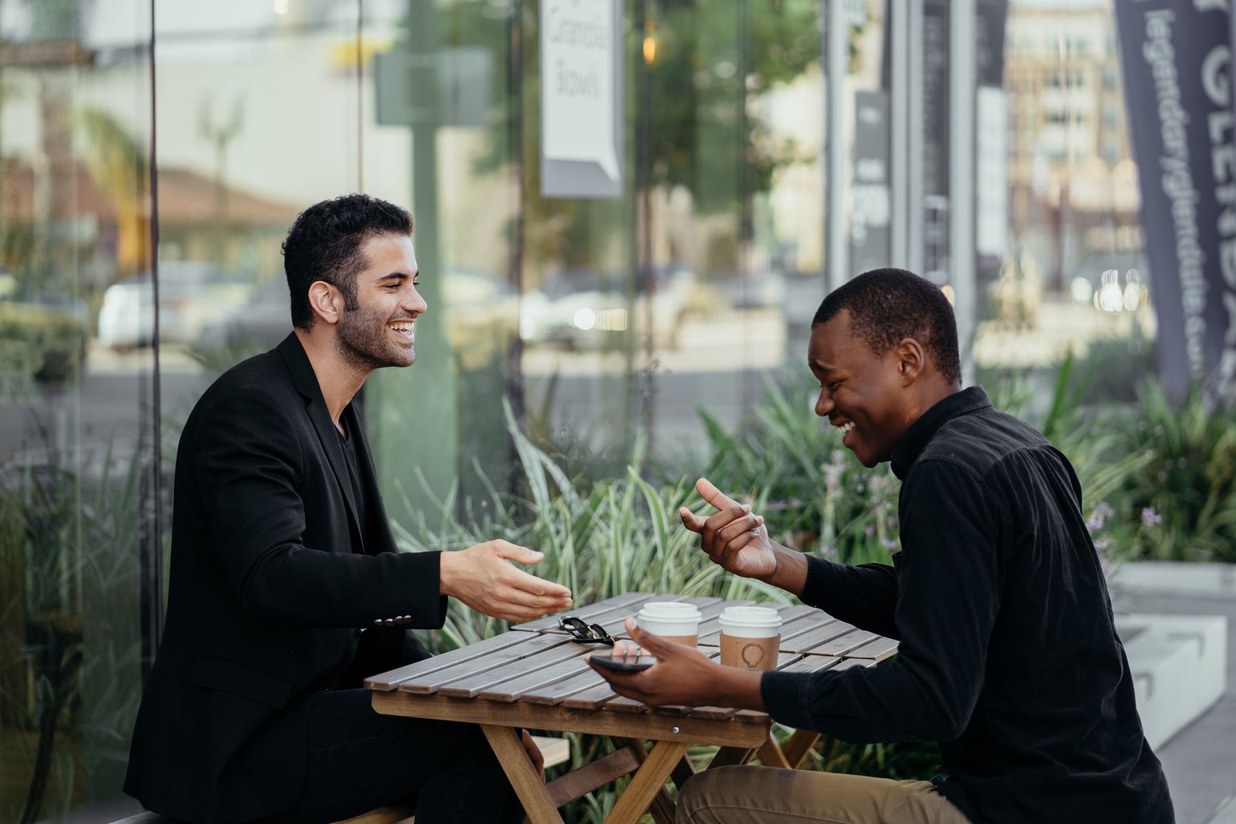 Two men smiling and talking over coffee at an outdoor café