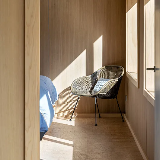 Light falling on a chair in the corner of a bedroom with light timber walls