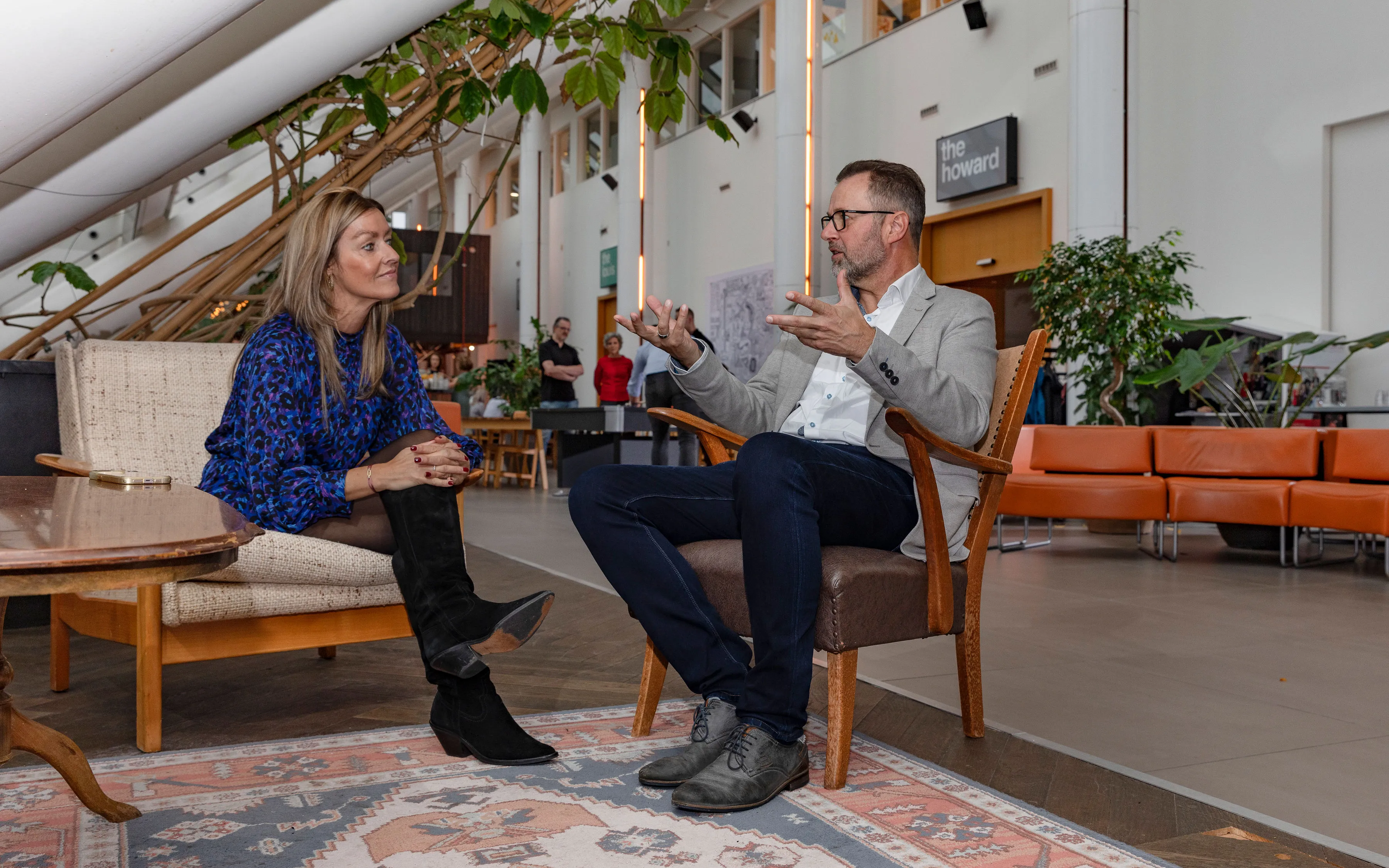 Twee mensen in een modern interieur in gesprek terwijl ze op stoelen zitten.