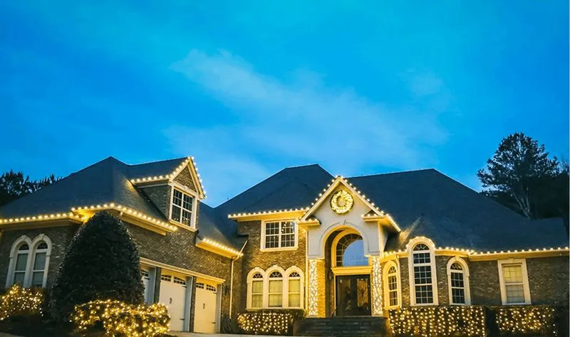 House decorated with professional Christmas lights under a blue evening sky