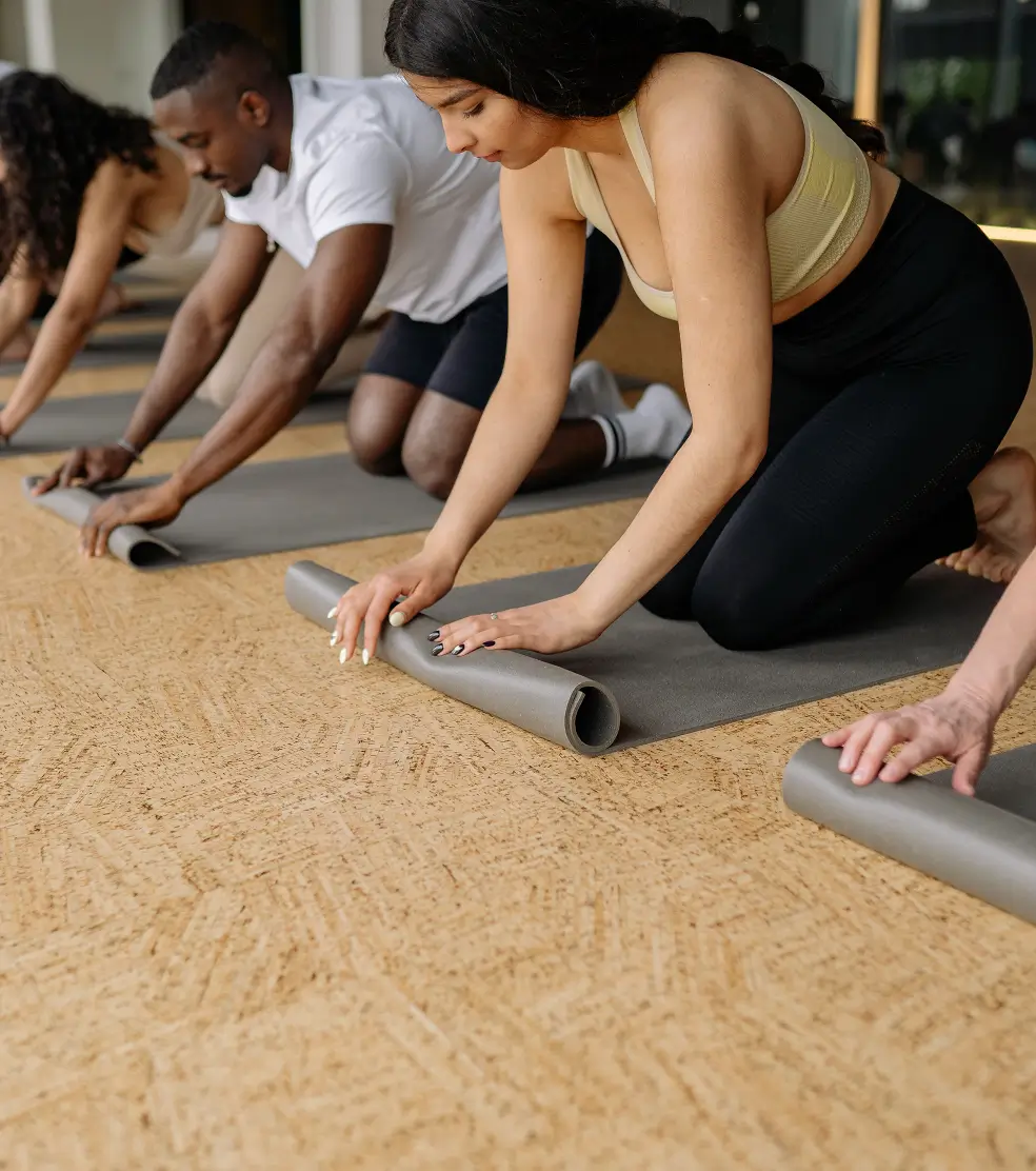 Students kneeling on the studio floor rolling up their yoga mats after class