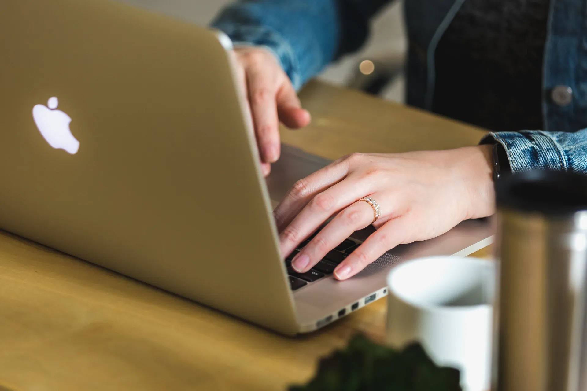 Person tippt auf einem MacBook an einem Holztisch – Symbolbild für digitale Entwicklung und E-Commerce