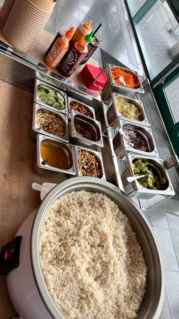 Zutaten-Theke mit frischen Toppings in Edelstahlbehältern und Reiskocher