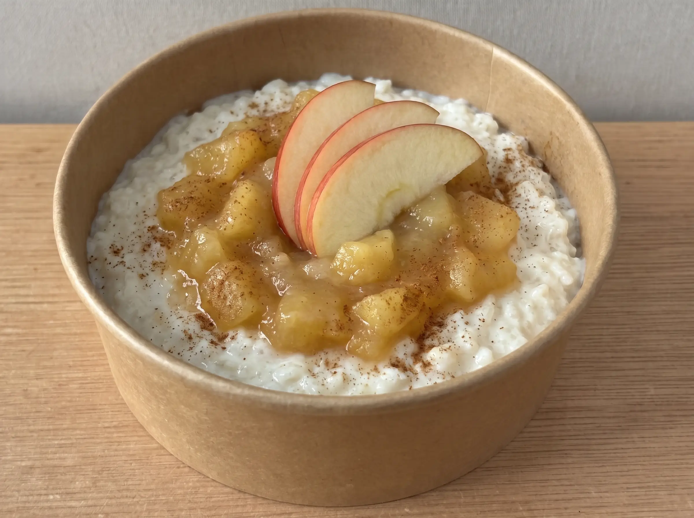 Milchreis-Bowl in brauner Pappschale mit Apfelmus, Zimt und frischen Apfelscheiben