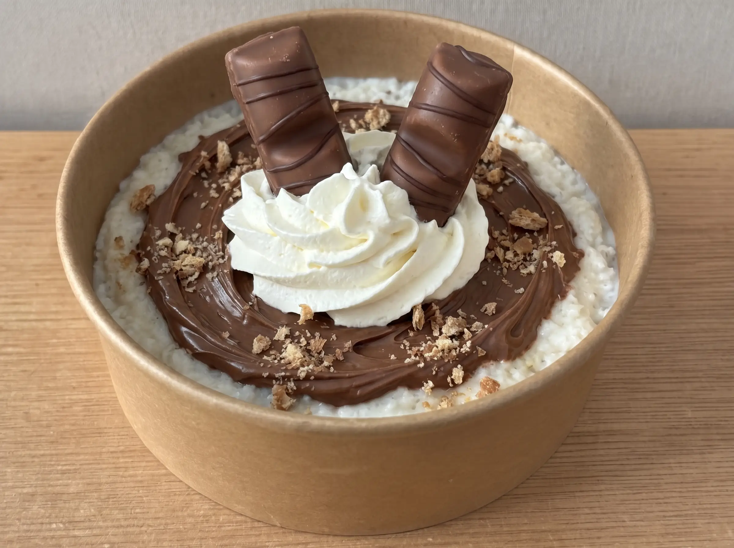 Milchreis-Bowl in brauner Pappschale mit Nutella, Sahnehaube und zwei Kinder-Bueno-Riegeln