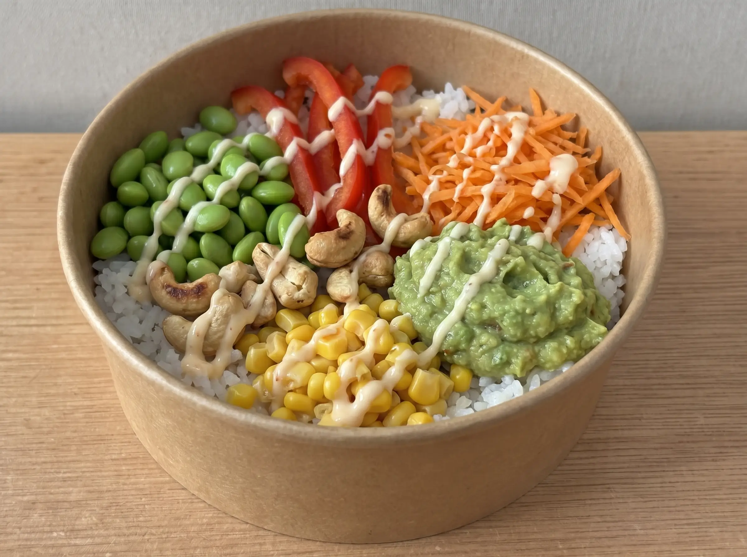 Veggie Crunch Bowl in brauner Pappschale: Sushireis, Edamame, Paprika, Möhren, Mais, Guacamole, Cashews und Sweet Chilli Mayo
