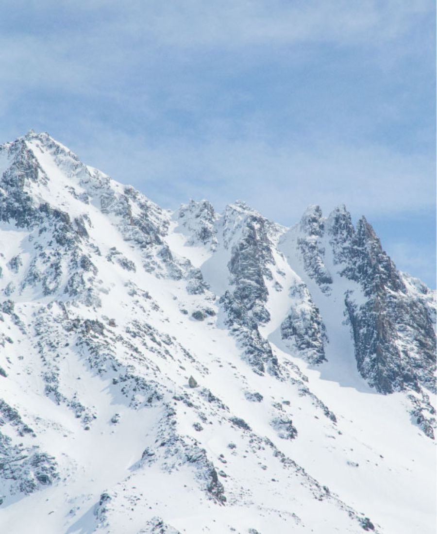 Montagne enneigée avec des pics rocheux sous un ciel bleu clair avec quelques nuages légers.