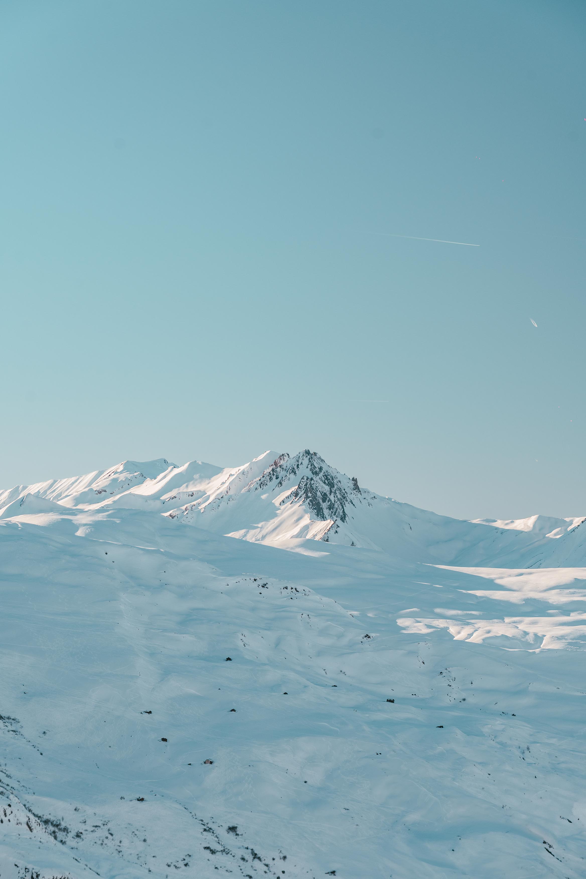 Vue panoramique de montagnes enneigées sous un ciel bleu clair, avec des sommets ensoleillés et une vaste étendue de neige blanche en arrière-plan.