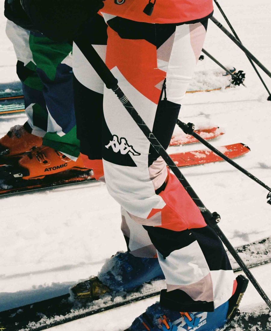 Personnes portant des pantalons de ski colorés avec des bâtons de ski, debout sur la neige avec des skis et des chaussures de ski visibles.