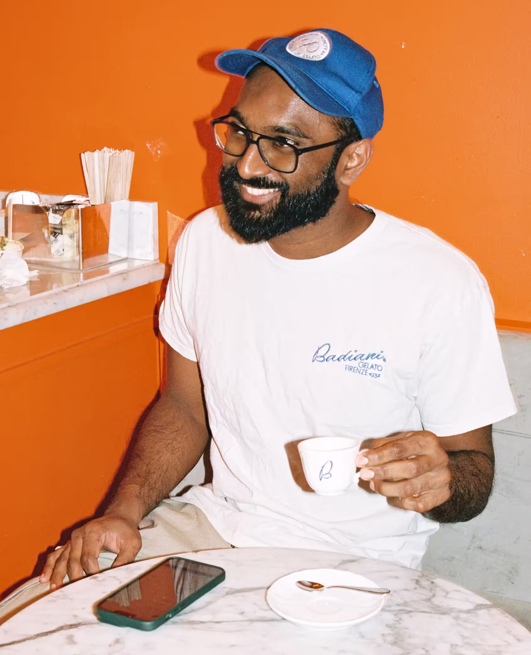 Smiling team member at Badiani Gelato enjoying an espresso at a marble table