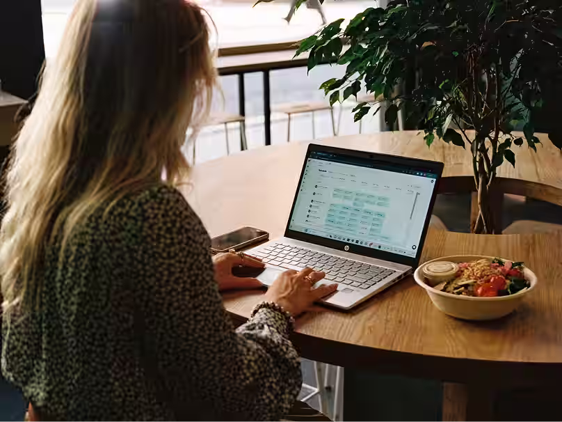 Restaurant manager using Nory AI software on a laptop at a café with a salad bowl nearby.