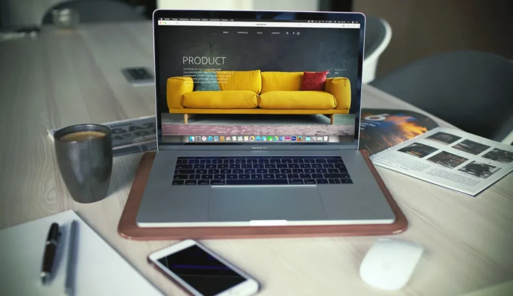 Laptop displaying a modern e-commerce website homepage with a yellow sofa product banner on screen
