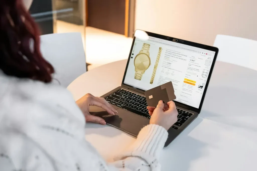 Woman shopping online on a laptop while holding a credit card on an e-commerce product page