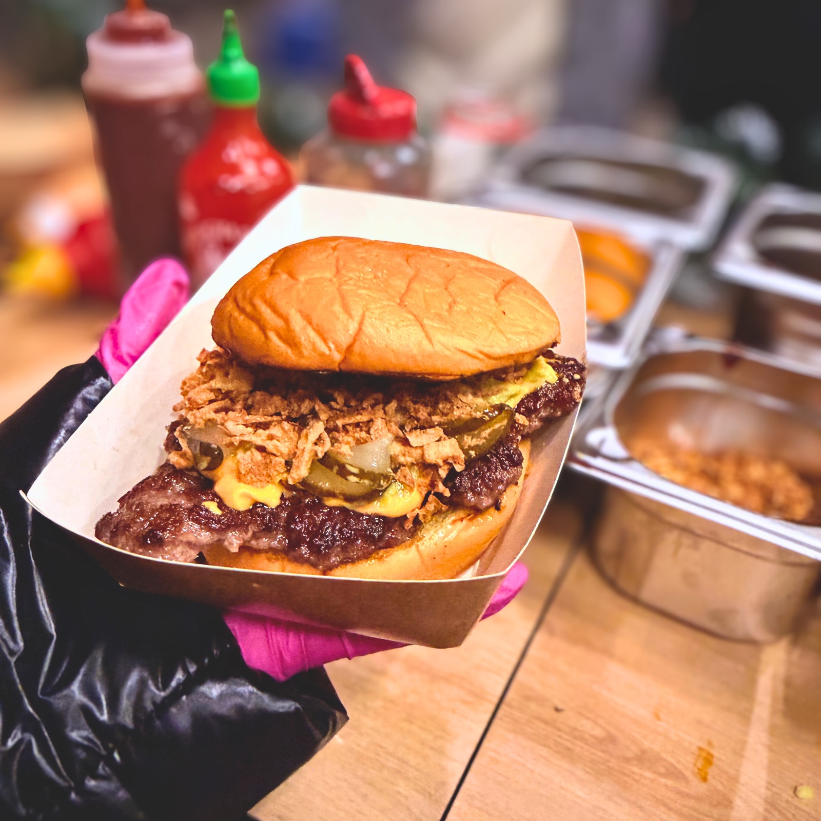 Smashed Burger mit Röstzwiebeln, Gurken und Chili-Cheese-Soße im Servierkarton