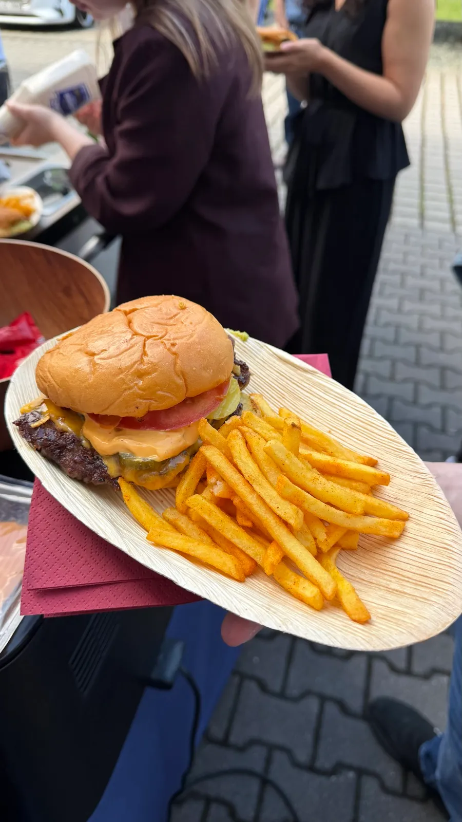 Burger mit Pommes auf dem Teller, im Hintergrund Gäste beim Event