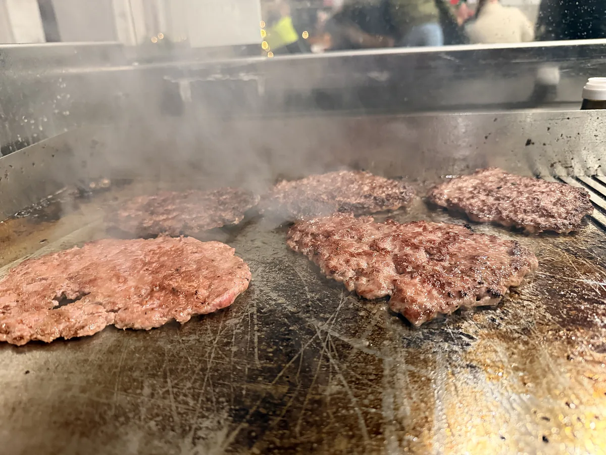 Patties werden live auf der heißen Platte gesmasht, darüber steigt Dampf auf