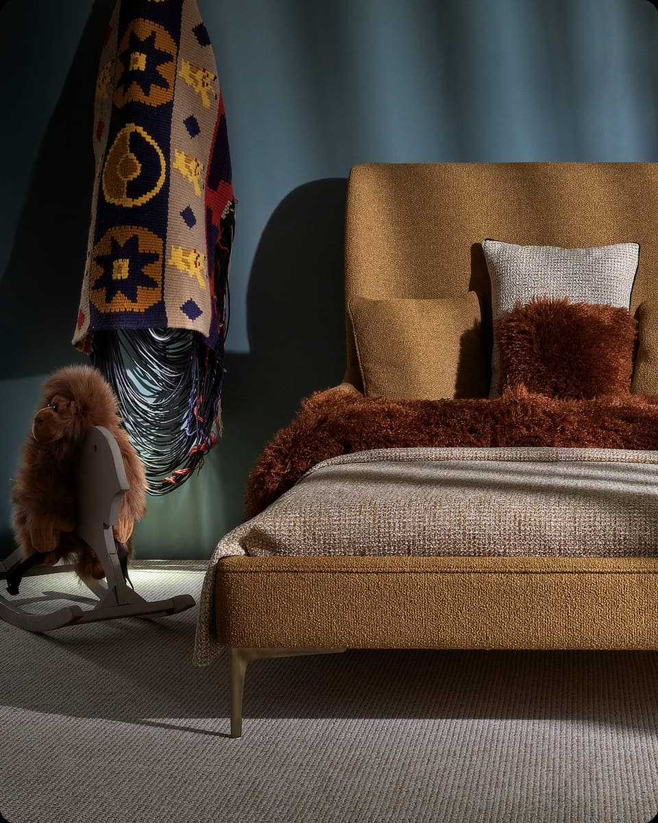 Brown upholstered bed with textured pillows and blanket next to a plush monkey on a wooden rocking horse.