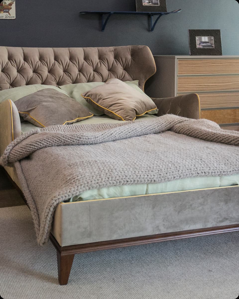 Modern bed with tufted headboard, two pillows, and thick knitted gray blanket in a bedroom.
