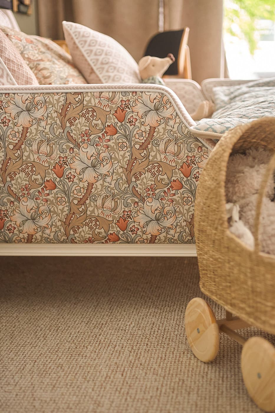 Floral patterned sofa with multiple pillows and a woven baby bassinet with wooden wheels.