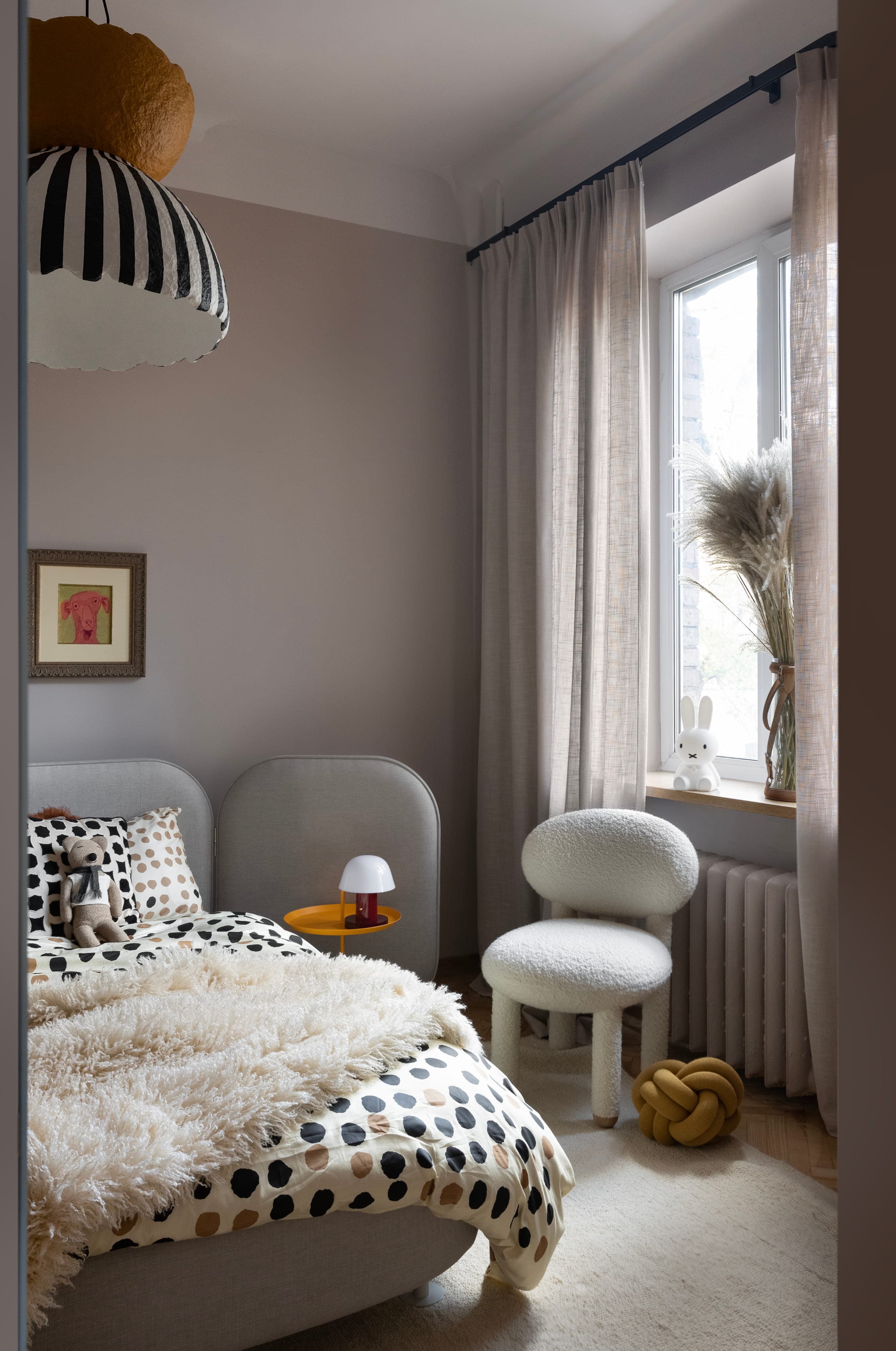 Cozy bedroom with polka dot bedding, fluffy throw, teddy on bed, modern chair, and soft natural light.
