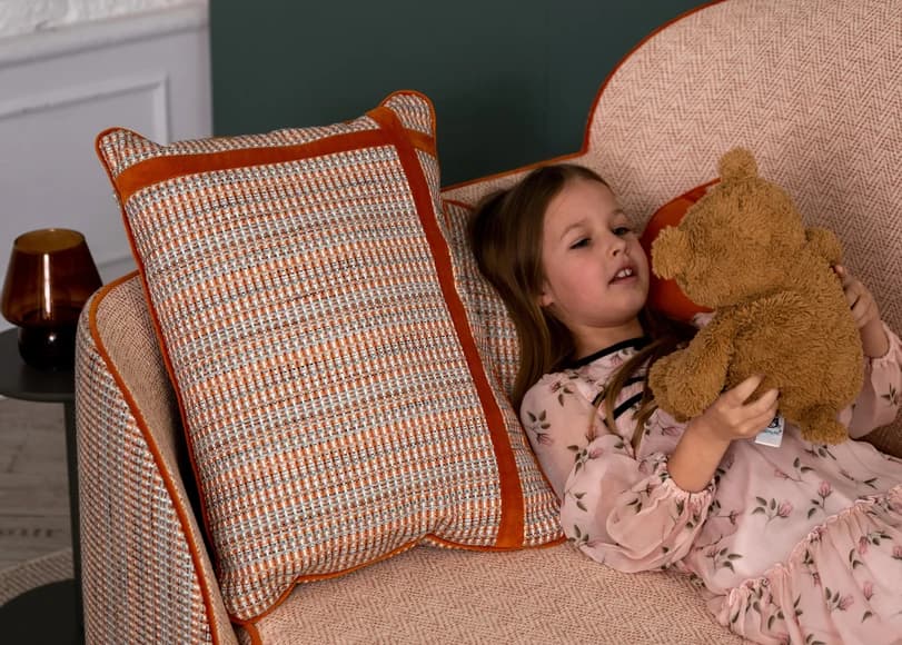 A girl is lying on a pink sofa, holding a soft teddy bear toy in her hands.