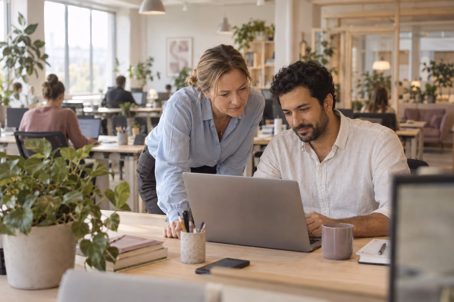 Eine Frau und ein Mann schauen gemeinsam auf einen Laptop in heller freundlicher Büro-Umgebung