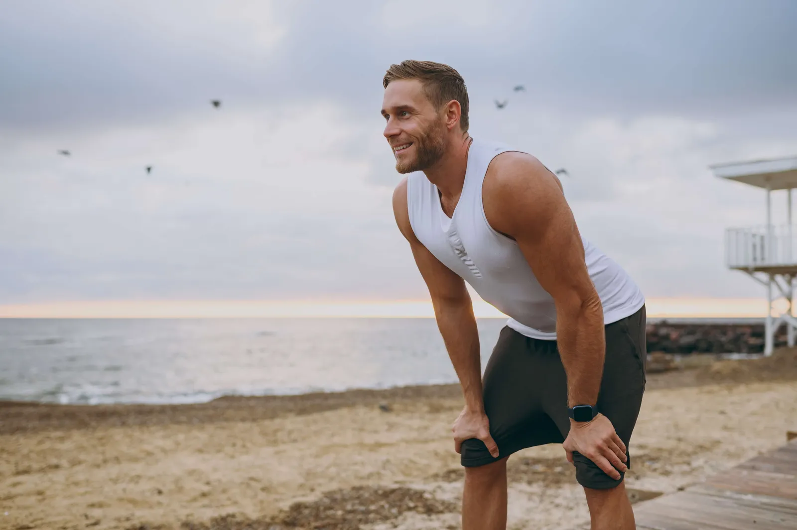 Man catching his breath with hands on knees during a run on the beach