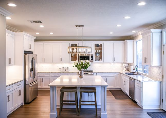 Bright modern kitchen with white cabinets, stainless steel fridge, island, and pendant light fixture.