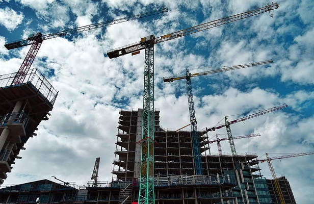 Several cranes above a multi-story building under construction against a cloudy sky.