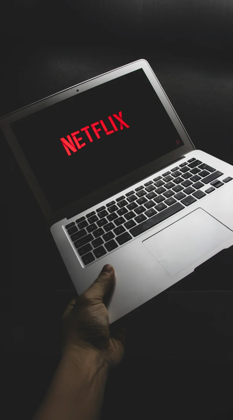Hand holding a laptop showing the Netflix logo on screen
