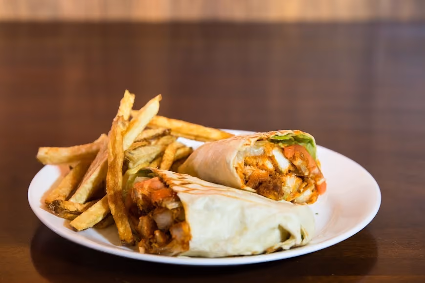 Plate with two halves of a grilled chicken wrap and a serving of French fries.