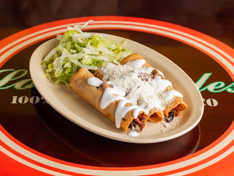 Plate with three rolled tacos topped with white sauce and cheese, served with shredded lettuce.