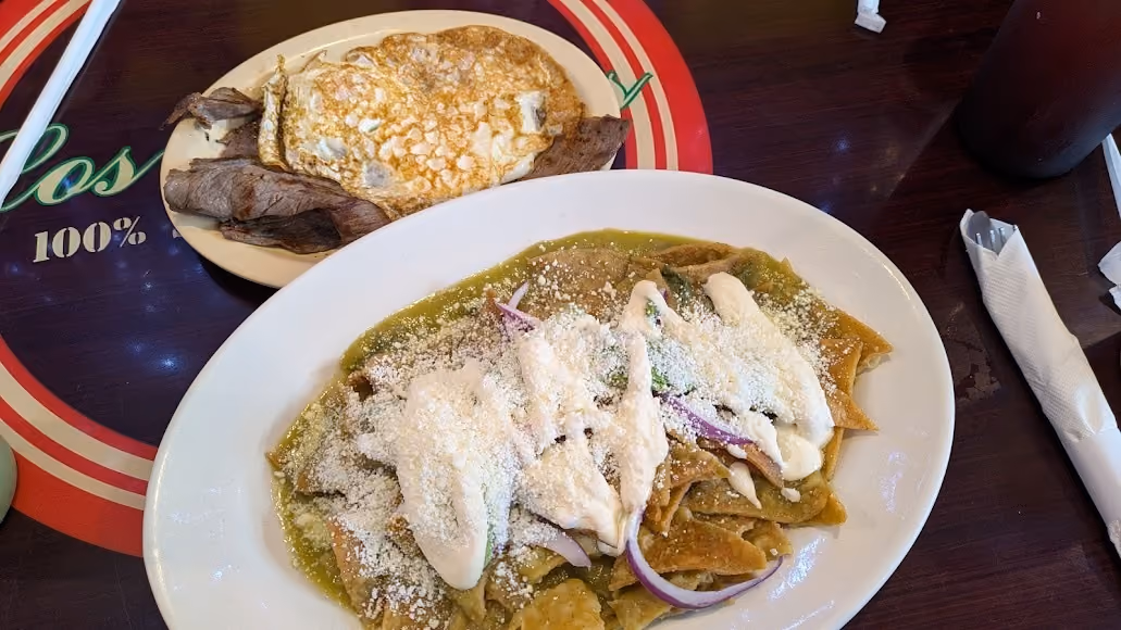 Plate of chilaquiles with green sauce, cream, cheese, and onions, and a plate with grilled steak and fried egg.