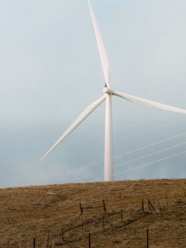 White wind turbine with three blades on a brown grassy hill under a cloudy sky.