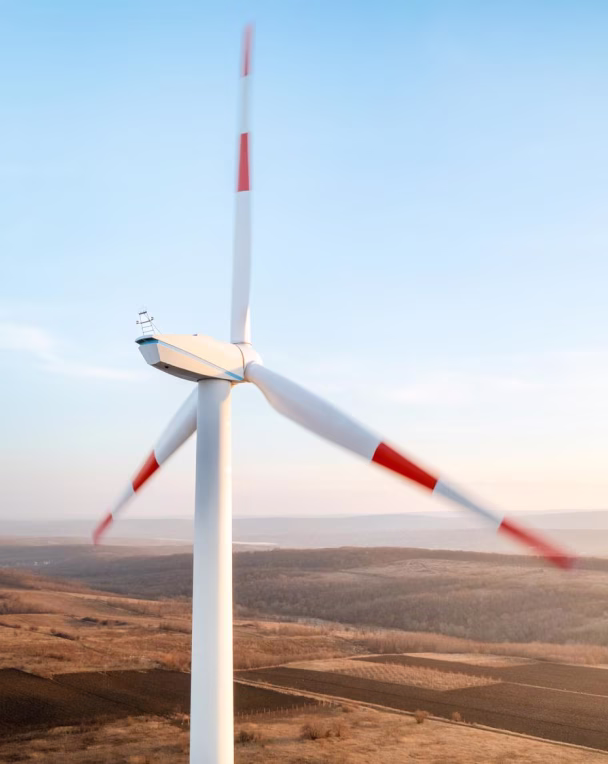 Close-up of a wind turbine with three rotating blades over a dry, open landscape under a blue sky.