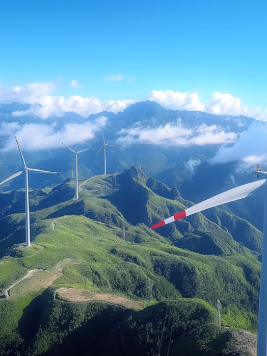 Wind turbines on green mountains under a blue sky with scattered clouds.